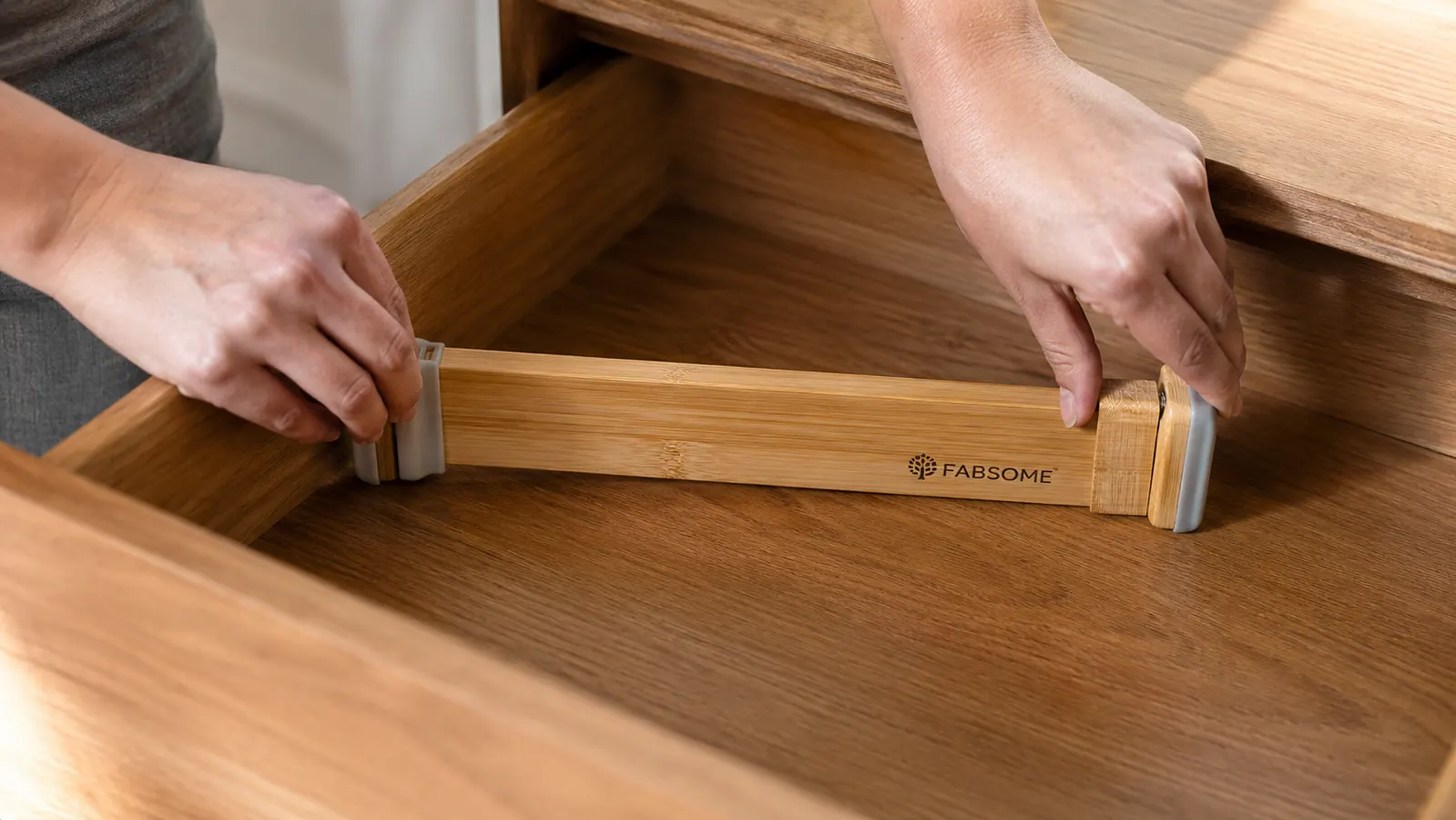 Hands pressing a spring-loaded bamboo divider into place inside a dresser drawer